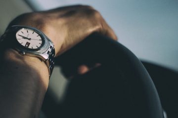 Hands with wristwatch on car wheel.