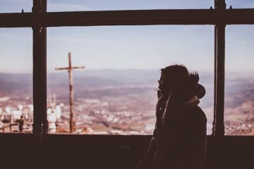 Woman standing at window with view of hills and city.